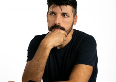 David Bello, en estudio, con fondo blanco, camiseta oscura y vaquero. Mirada lateral medio cuerpo.